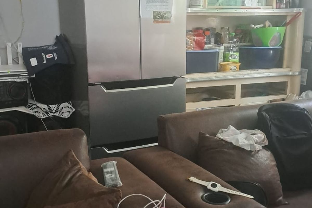 A cluttered living area showing a sofa and storage shelving with visible electrical wiring on the wall.