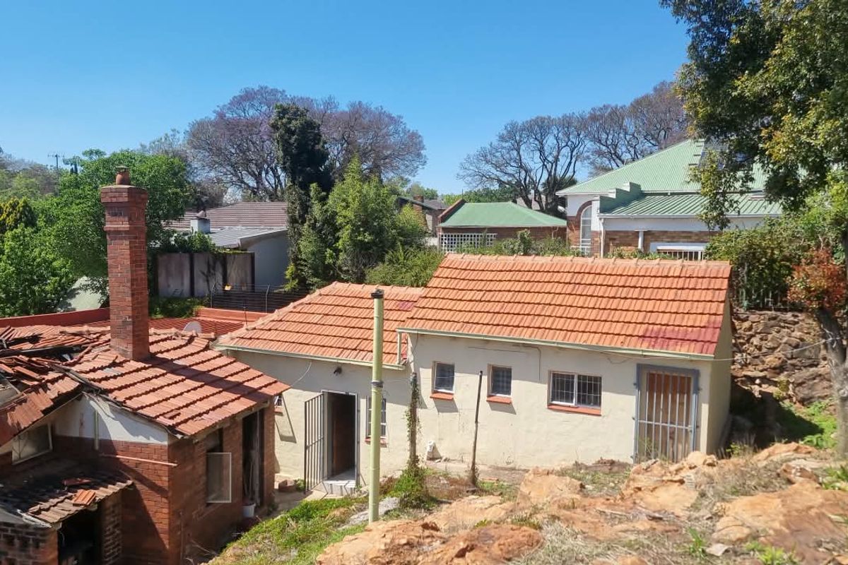 Rear view of the property showing multiple outbuildings with terracotta tiled roofs, brick chimney, and security features, set against a natural rocky landscape.