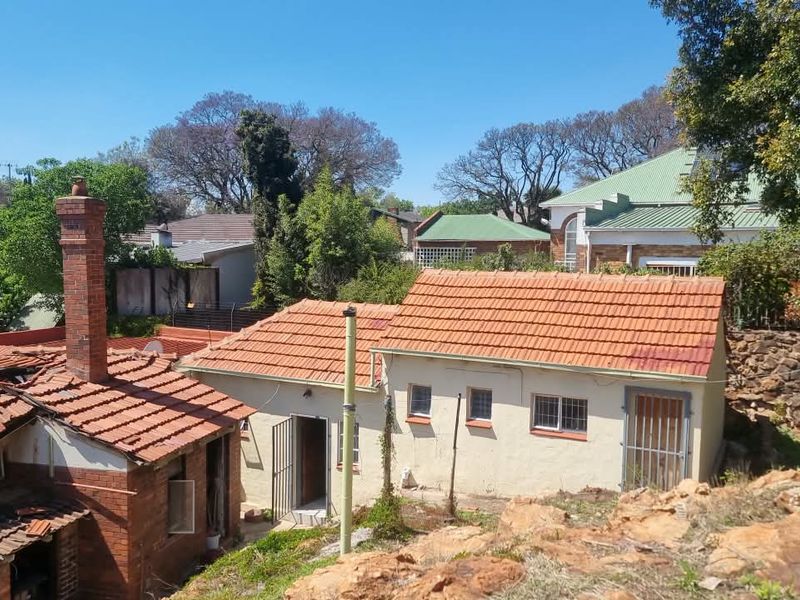 Rear view of the property showing multiple outbuildings with terracotta tiled roofs, brick chimney, and security features, set against a natural rocky landscape.