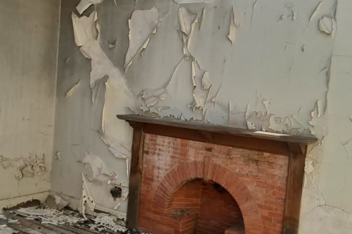 A severely fire-damaged living room featuring a brick fireplace and exposed roof rafters, requiring extensive structural renovation and repair.