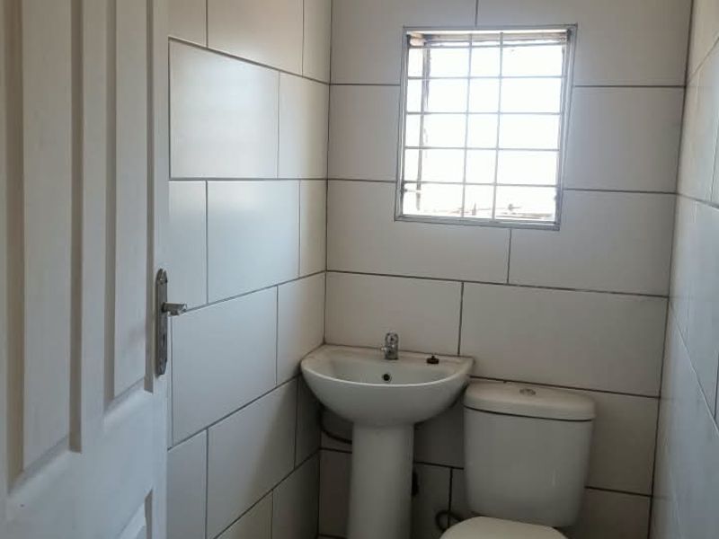 A compact bathroom featuring a pedestal basin, toilet, and wall-mounted shower head with full-height wall tiling and a floor drain.