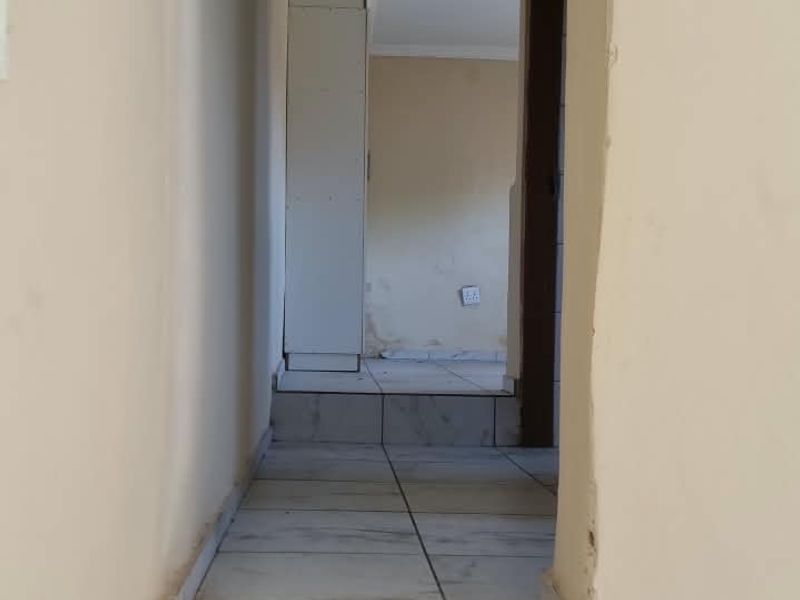A narrow hallway featuring tiled flooring and a built-in cupboard, showing signs of wear on the walls and door frames.