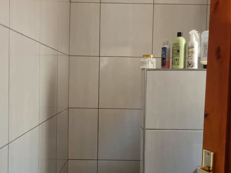 A small tiled bathroom shower area featuring white wall tiles and a damaged ceiling section requiring repair.