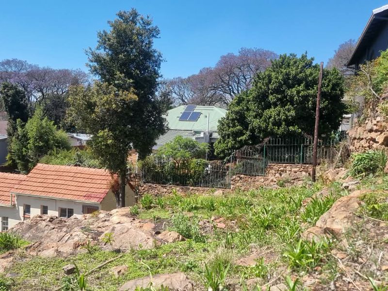 A view of the rear property grounds featuring a rocky slope, stone retaining wall, and neighboring houses with solar panels installed on the roof.