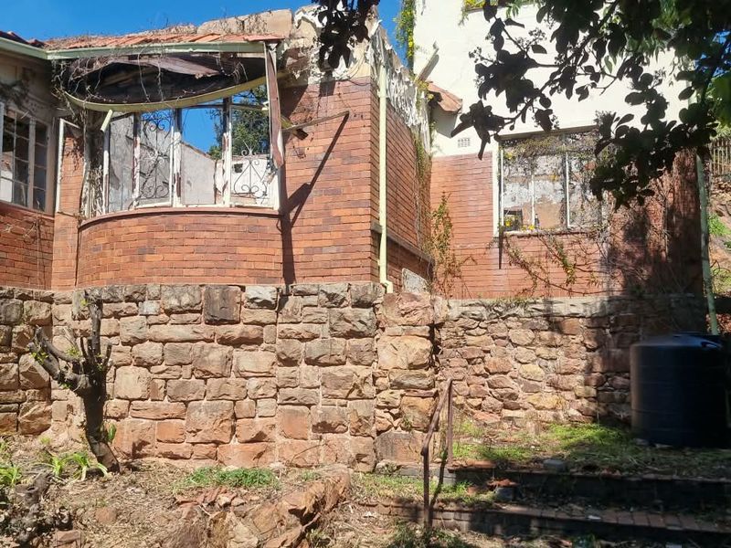 Rear exterior view of a property showing significant structural damage, including a collapsed roof section and deteriorated brickwork requiring major renovation.