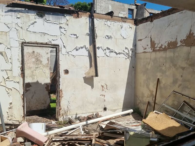 A severely damaged interior space showing significant structural deterioration, missing roof, and extensive wall damage, requiring major renovation or demolition.