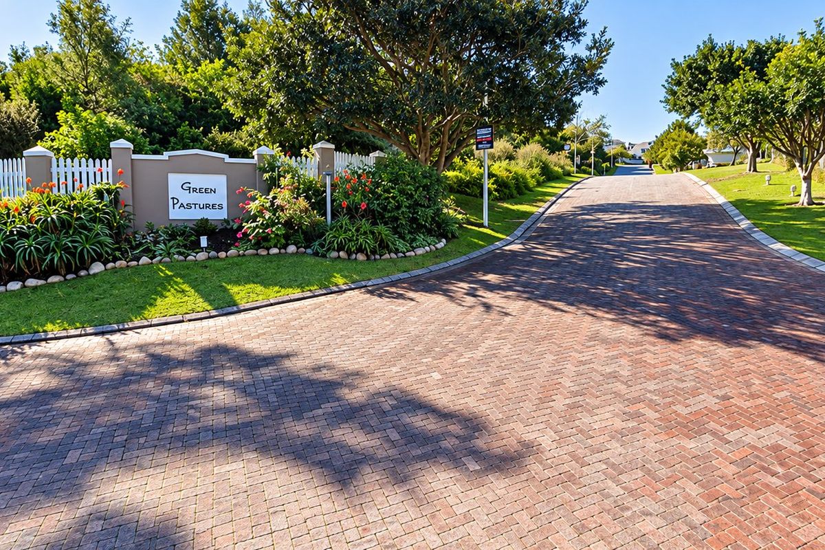 A well-maintained entrance to the Green Pastures estate, featuring a paved driveway, established trees, and landscaped garden beds.