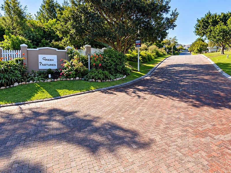 A well-maintained entrance to the Green Pastures estate, featuring a paved driveway, established trees, and landscaped garden beds.