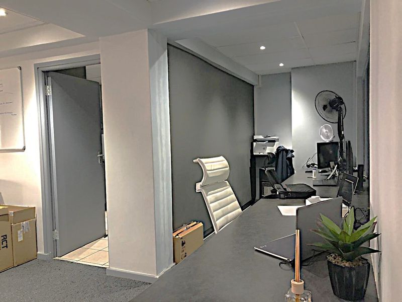 A functional commercial office space featuring a built-in desk, recessed ceiling lighting, and neutral finishes, suitable for a professional work environment.