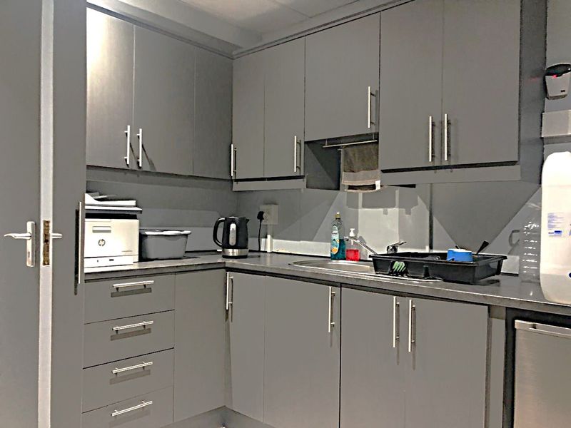 A compact kitchen area featuring modern grey cabinetry, laminate countertops, and a stainless steel sink with a mixer tap.