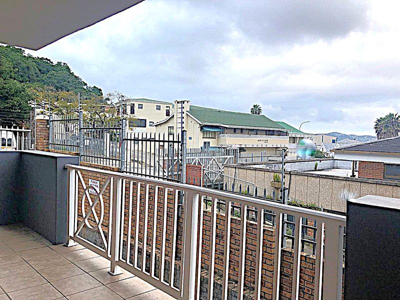 A covered balcony area featuring tiled flooring and a metal balustrade, overlooking the surrounding commercial property and neighborhood.