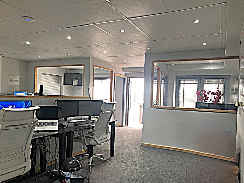 A functional commercial office space featuring internal glass partitions, suspended ceilings with recessed lighting, and carpeted flooring.