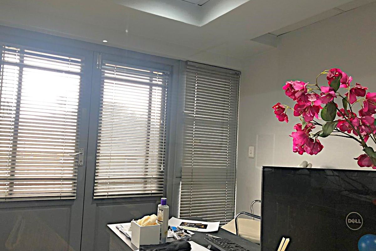 A professional office space featuring recessed ceiling lighting, venetian blinds, and double glass doors providing natural light.