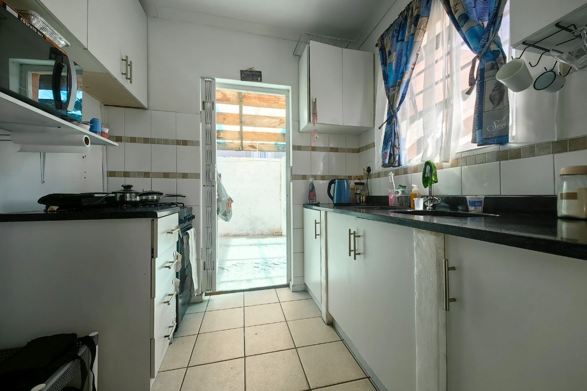 A functional kitchen featuring white cabinetry, dark countertops, tiled backsplash, and direct access to an outdoor area through a security gate.