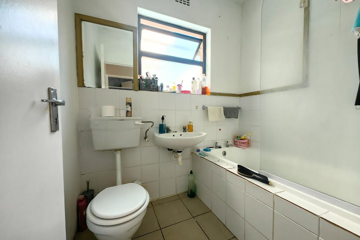 A functional bathroom featuring a bathtub with a glass screen, wall-mounted basin, and toilet, finished with white wall tiles and floor tiling.