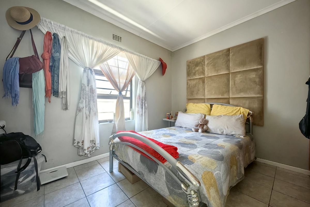 A bedroom featuring tiled flooring, a wall-mounted headboard, and a window fitted with security bars.