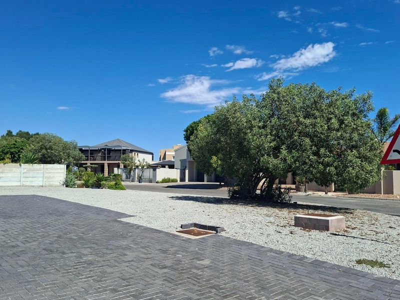 A vacant residential plot featuring a paved driveway, gravel landscaping, and established boundary walls in a quiet suburban street setting.