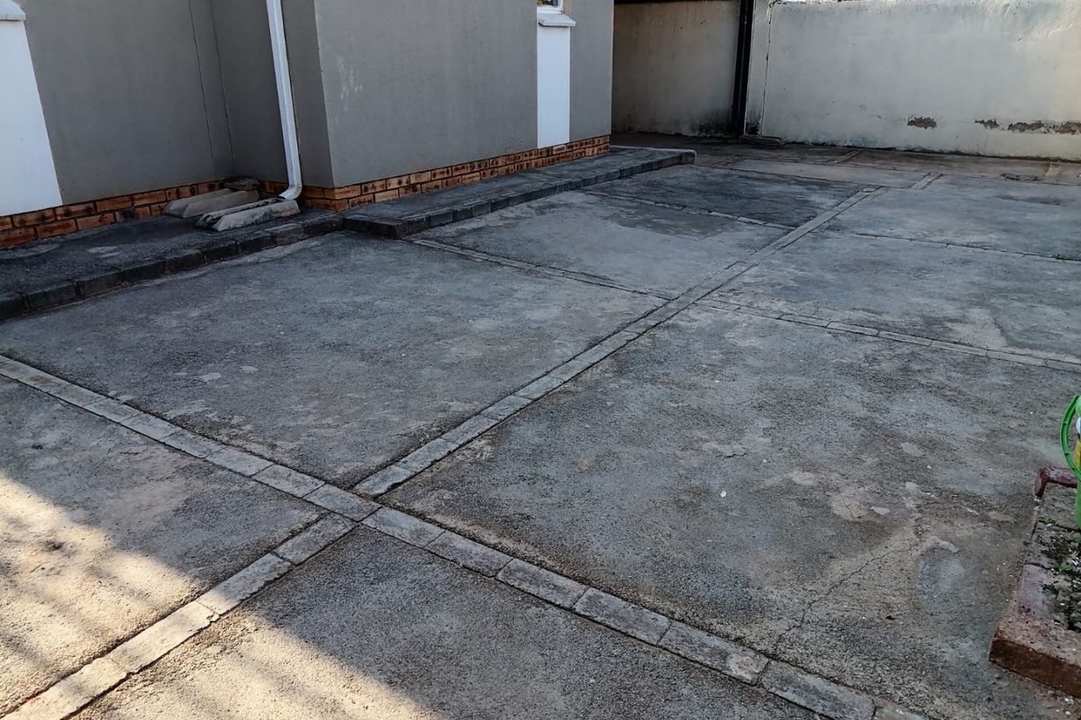 A paved rear courtyard area featuring concrete paving with brick detailing, adjacent to the main building structure and a perimeter boundary wall.