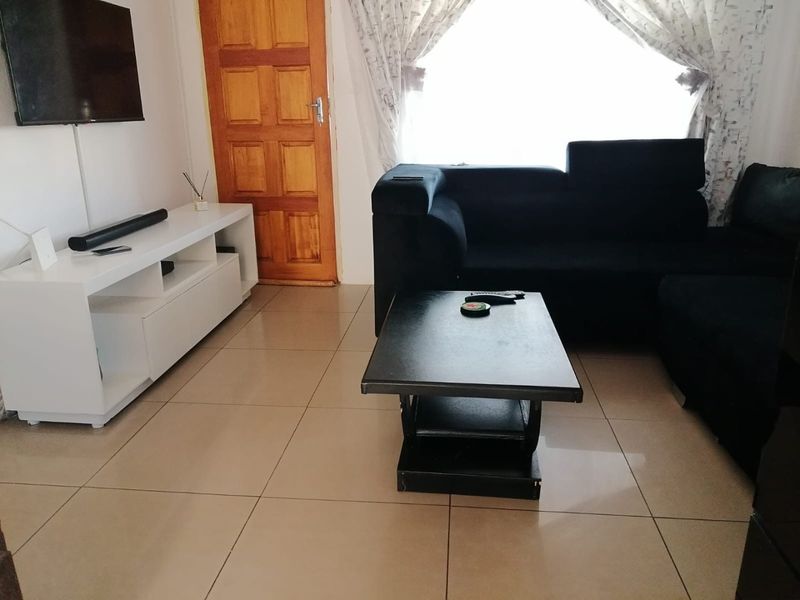 A living room featuring neutral tiled flooring and a solid timber door, providing a functional and well-lit space.