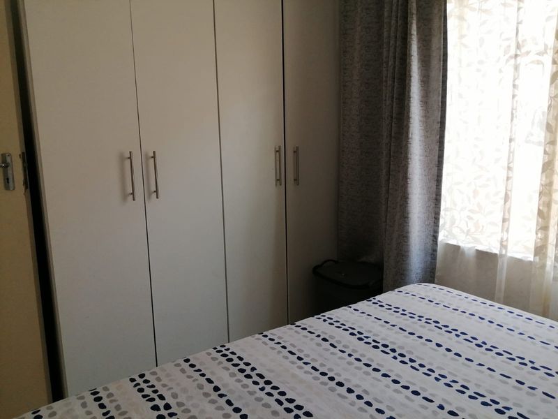 A bedroom featuring white built-in cupboards with modern handles and natural light filtering through window curtains.
