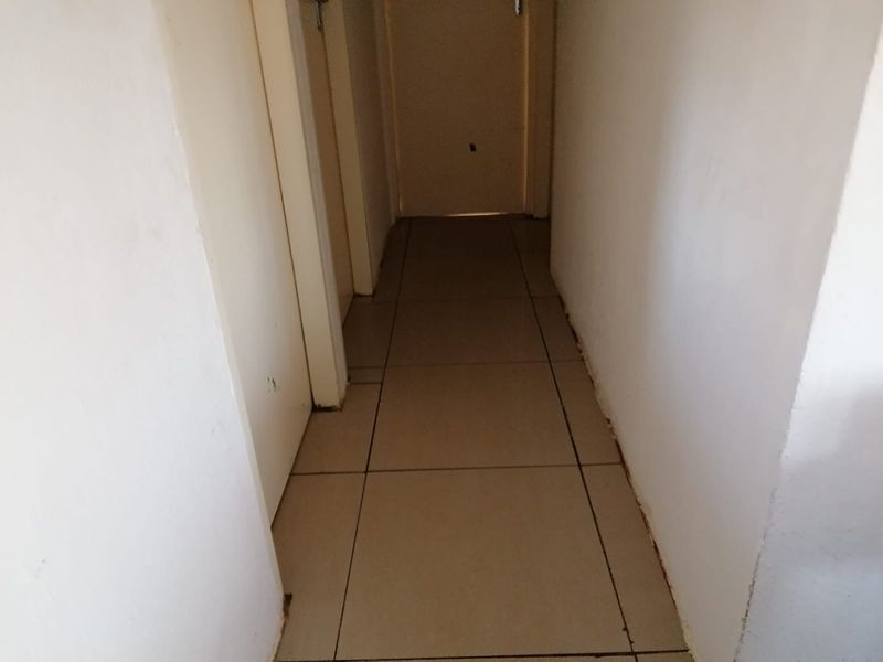 A narrow interior hallway featuring neutral floor tiles and multiple internal doors, showing signs of wear on the walls and skirting boards.