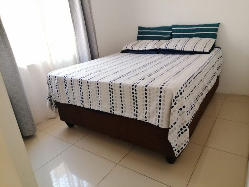 A bedroom featuring neutral tiled flooring and natural light from the window.