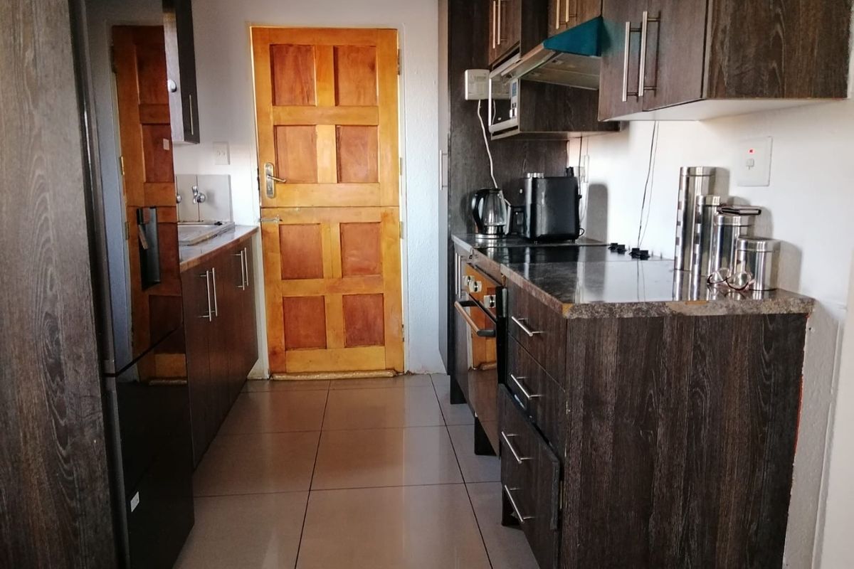 A galley-style kitchen featuring dark wood-finish cabinetry, laminate countertops, built-in oven, extractor fan, and tiled flooring with a timber door leading outside.