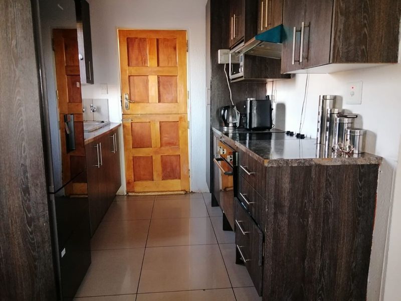 A galley-style kitchen featuring dark wood-finish cabinetry, laminate countertops, built-in oven, extractor fan, and tiled flooring with a timber door leading outside.