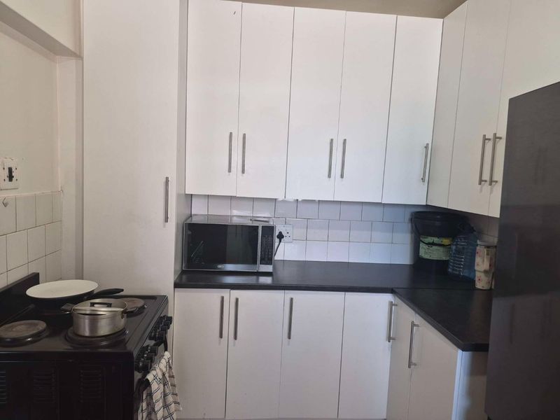 A functional kitchen featuring white built-in cabinetry, dark countertops, and a tiled backsplash, providing a practical workspace for daily cooking needs.