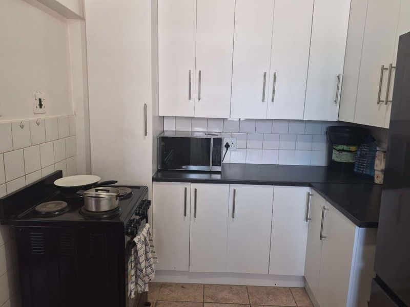 A functional kitchen featuring white built-in cabinetry, dark laminate countertops, tiled backsplash, and tiled flooring with an integrated electric stove.