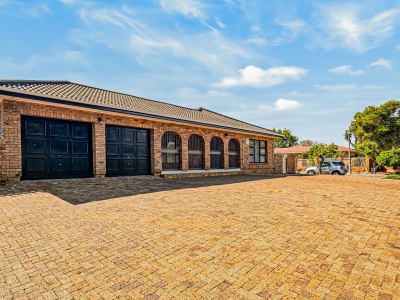Front exterior view of a brick house featuring a spacious paved driveway, double garage, and arched window detailing.