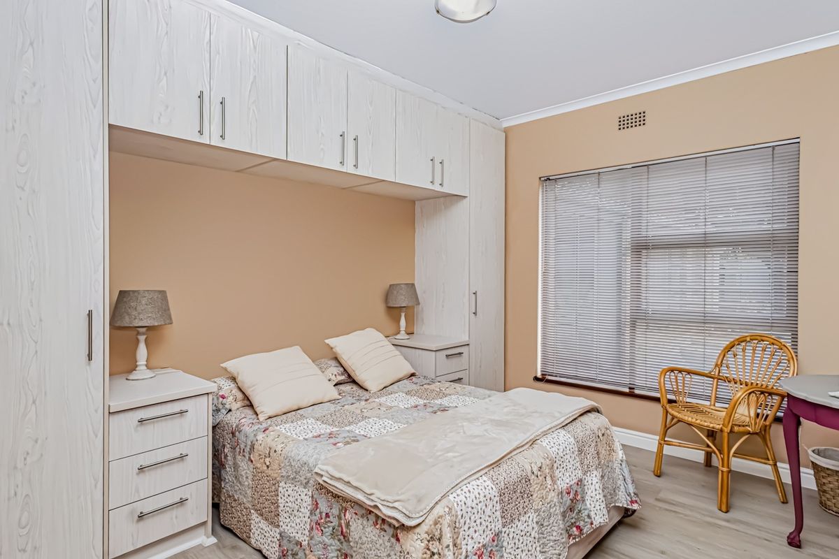 A well-maintained bedroom featuring extensive built-in cabinetry, laminate flooring, and large windows with fitted venetian blinds.