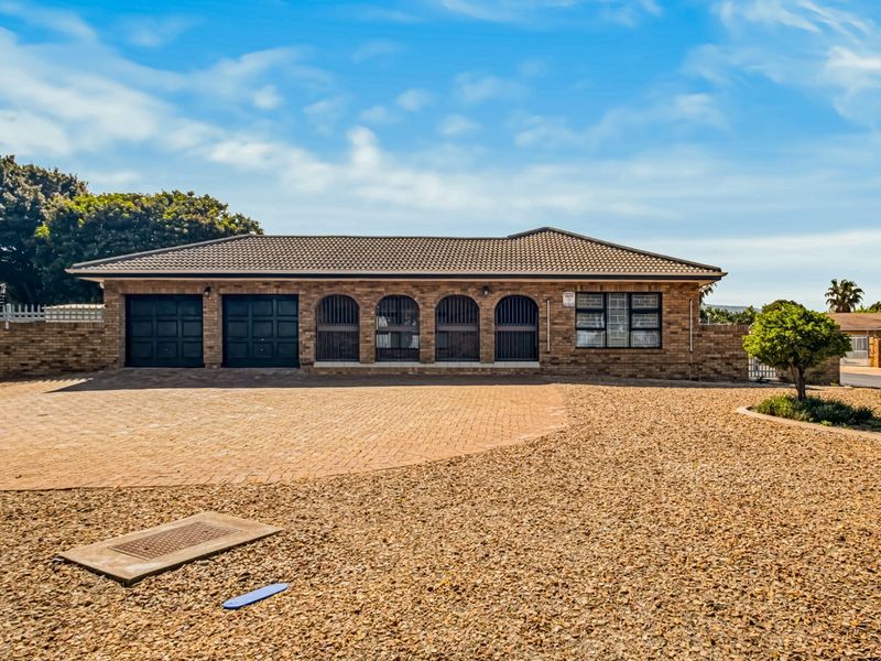 Front elevation of a single-story brick house featuring a tiled roof, double garage, and arched window detailing with a spacious paved driveway.