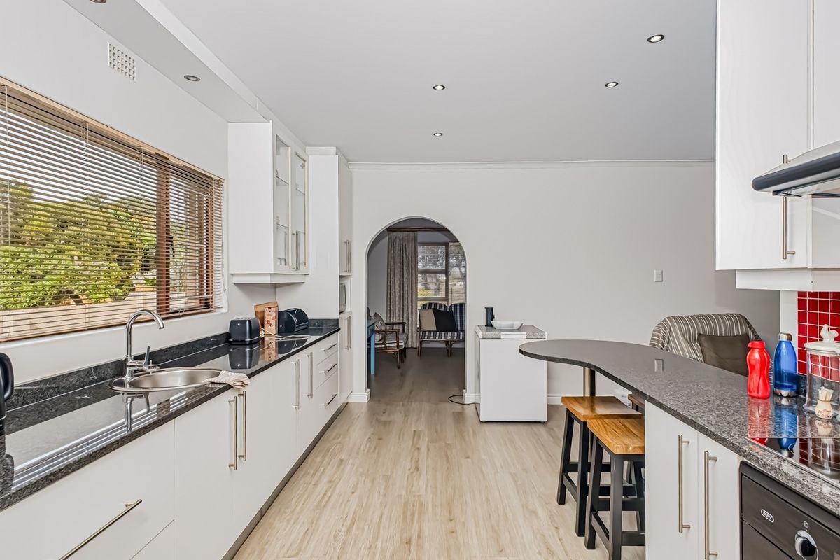 Modern kitchen featuring white cabinetry, granite countertops, stainless steel fixtures, and an integrated oven, leading through an archway to the adjacent living area.