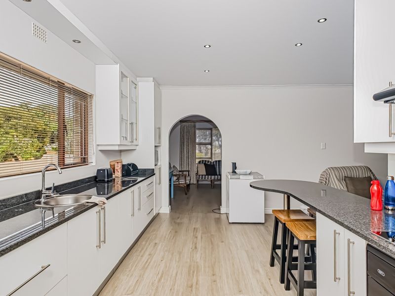 Modern kitchen featuring white cabinetry, granite countertops, stainless steel fixtures, and an integrated oven, leading through an archway to the adjacent living area.