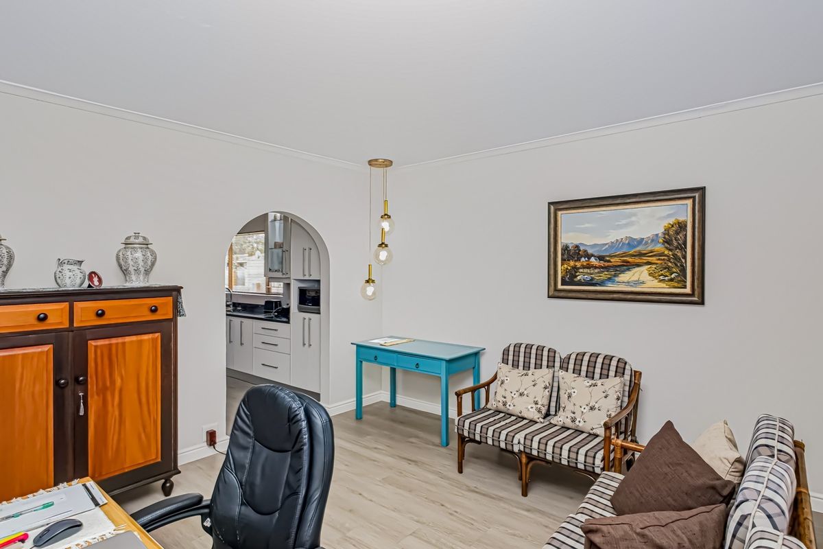 A well-maintained living area featuring laminate flooring, coving, and an arched doorway leading to the kitchen, with neutral wall finishes.