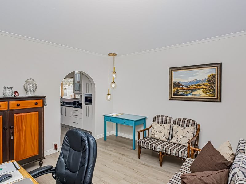 A well-maintained living area featuring laminate flooring, coving, and an arched doorway leading to the kitchen, with neutral wall finishes.