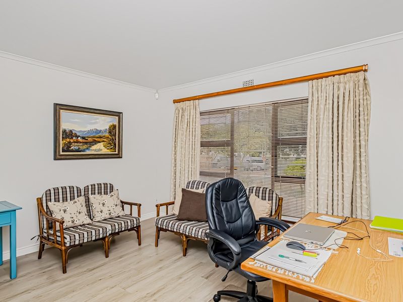 A bright home office featuring light-toned laminate flooring, coved cornicing, and large windows fitted with venetian blinds and curtains.