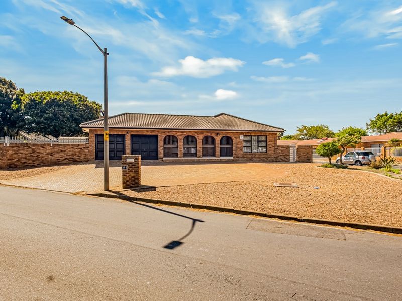 A well-maintained single-story brick house featuring a tiled roof, paved driveway, and secure garage access, situated on a corner plot.
