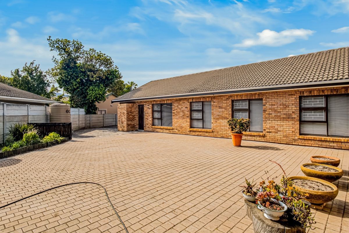 A well-maintained rear exterior view featuring a spacious paved courtyard, brick facade, and secure boundary walling.