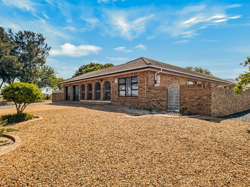 A well-maintained single-story brick house featuring a hipped roof, arched window detailing, and a spacious gravel driveway with a surrounding brick boundary wall.