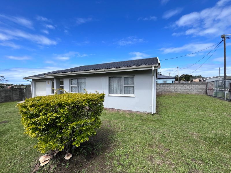 Rear view of a single-story house featuring a tiled roof, aluminium windows, and a surrounding concrete block boundary wall with a lawn area.