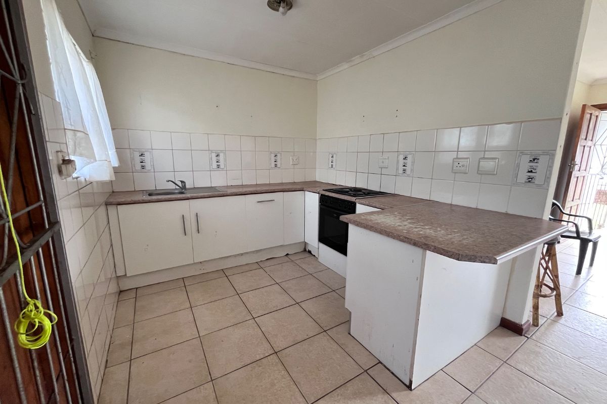 A functional kitchen featuring white cabinetry, laminate countertops, a built-in oven and hob, and tiled splashbacks. The space is currently vacant and ready for updates.