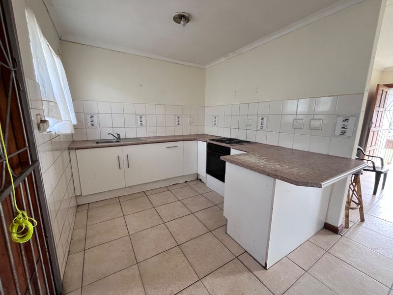 A functional kitchen featuring white cabinetry, laminate countertops, a built-in oven and hob, and tiled splashbacks. The space is currently vacant and ready for updates.