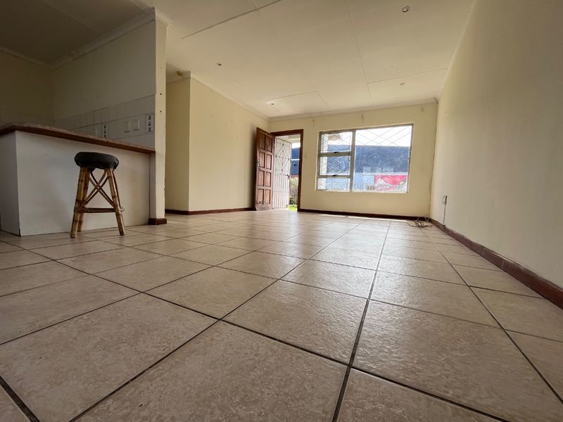 An open-plan living area featuring tiled flooring, a breakfast counter, and direct access to the exterior through a security gate.