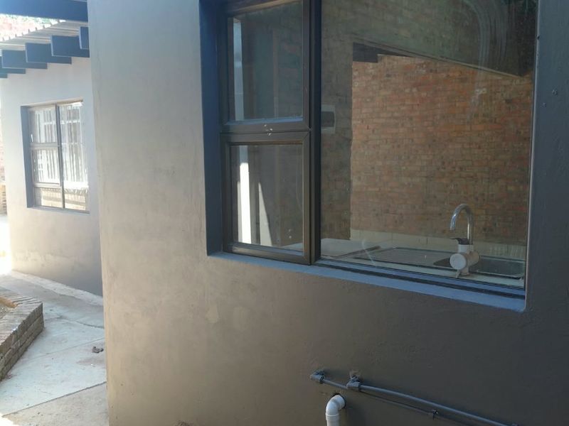 Rear exterior view showing dark painted walls, aluminium window frames, and exposed brickwork with external plumbing fixtures.