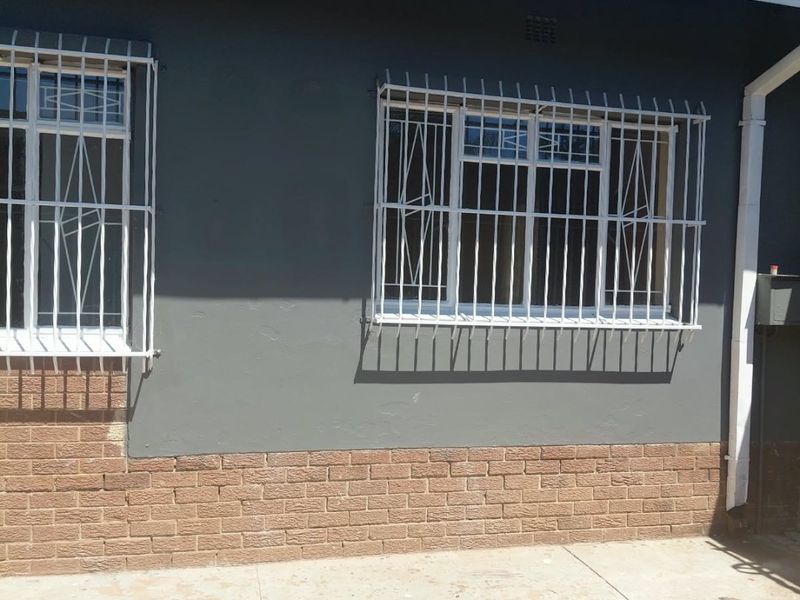 Rear exterior view of the property featuring dark painted walls, brick base detailing, security bars on windows, and concrete paving.