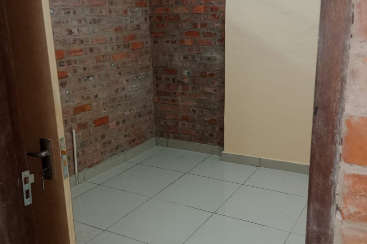 An empty bedroom featuring exposed brick walls and ceramic floor tiles, requiring finishing touches to complete the space.