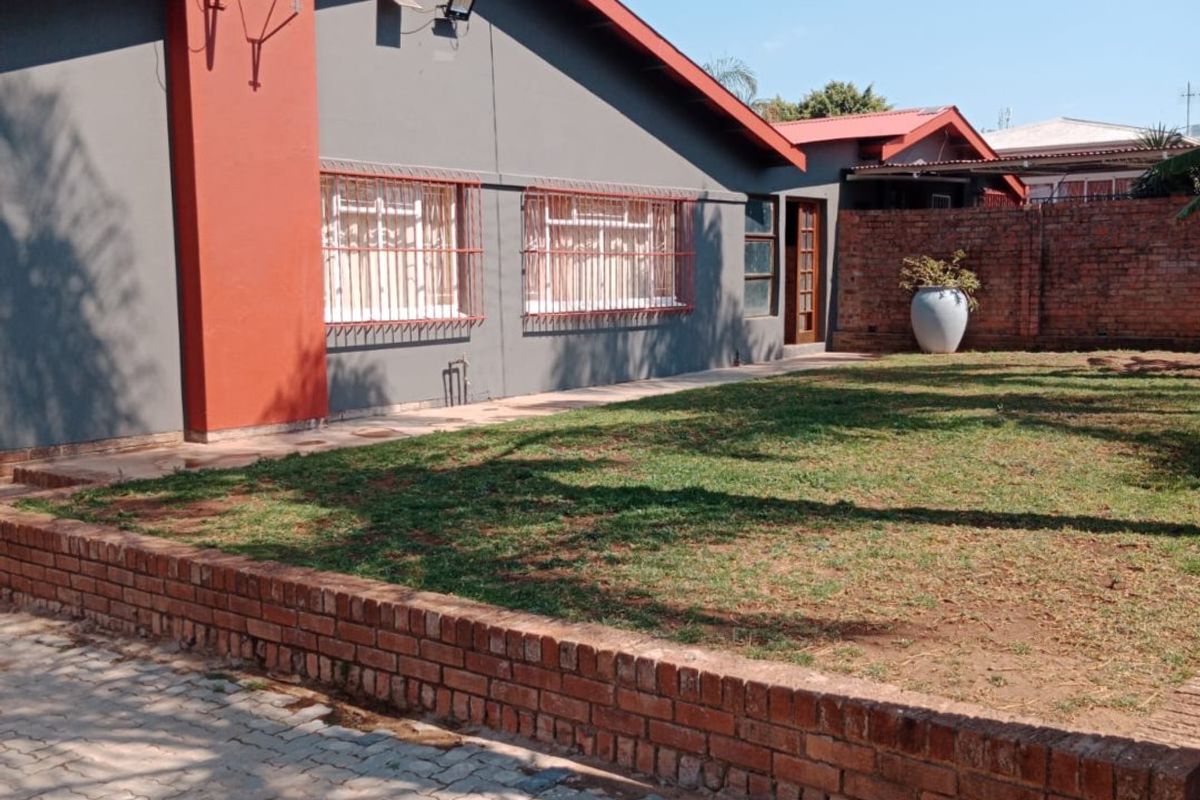 Rear view of the property featuring a paved driveway, brick retaining wall, and a private garden area with security bars on the windows.