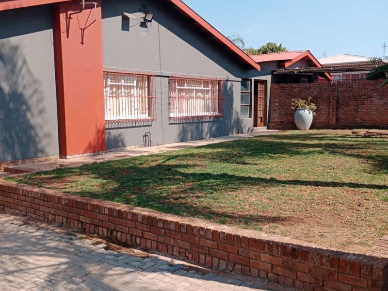 Rear view of the property featuring a paved driveway, brick retaining wall, and a private garden area with security bars on the windows.
